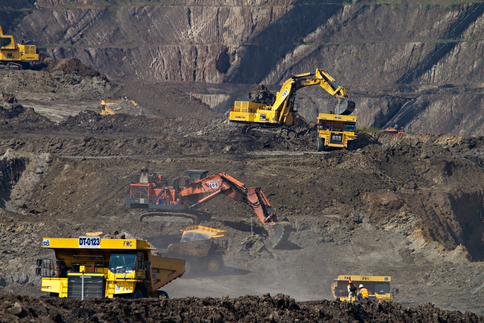 A fleet of excavators and articulated haul trucks working a large benched cut