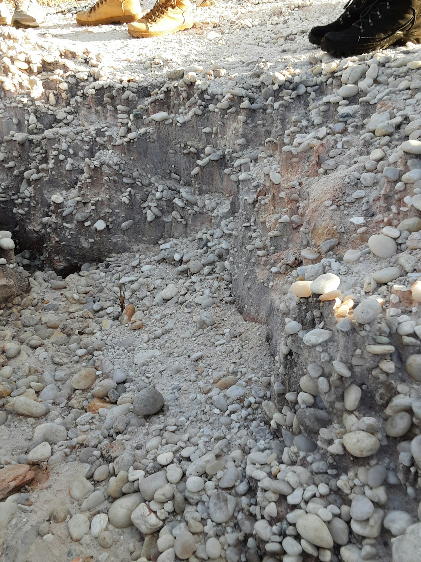 An open utility trench cut through layered river cobble and clay